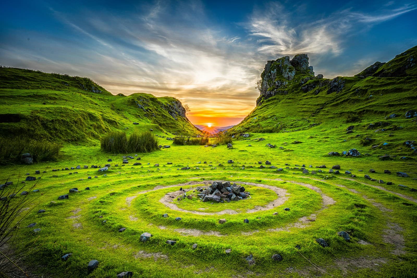 Sunset over green hills with a stone labyrinth path in a quiet valley