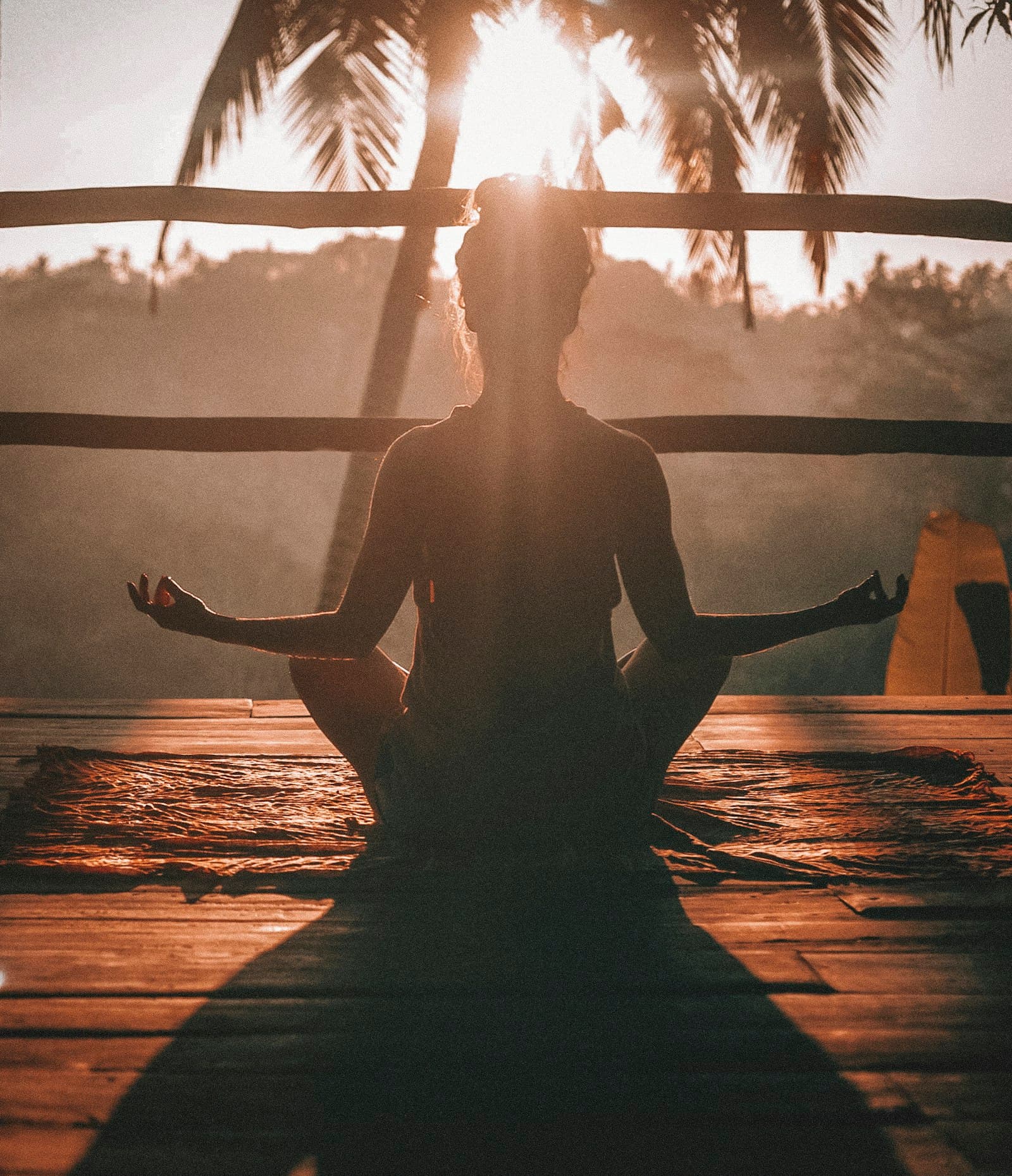 Warm sunrise light on a wooden deck, figure in silhouette sitting on a mat in a quiet meditative pose